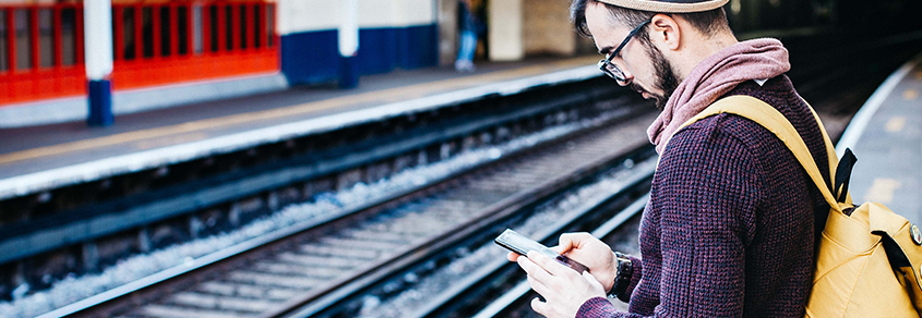 Tourist waiting on train platform looking at his mobile phone
